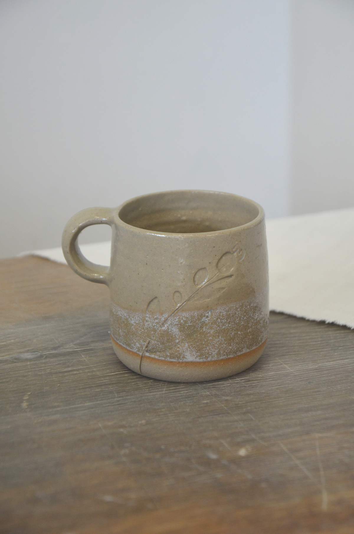 Tasse à anse beige et blanche, décor d'un brin végétal.