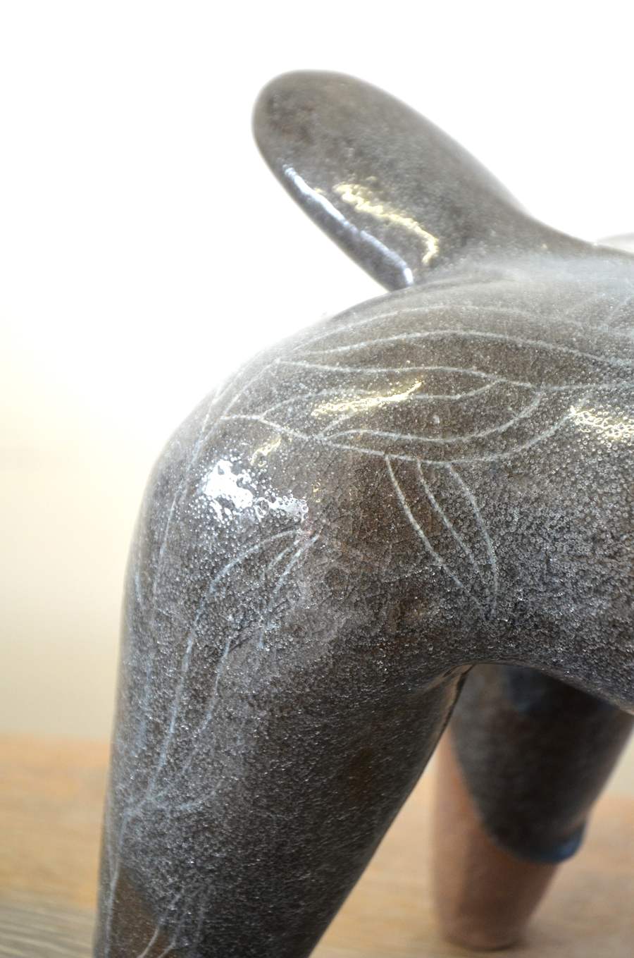 Détail de la surface grise et brillante d'une pièce, parcourue de feuillages clairs.