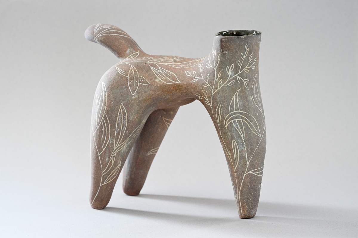 Pièce brune évoquant un animal à quatre pattes, ornée de feuillages blancs, sur fond gris.